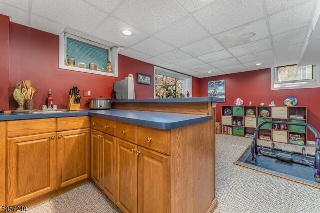 kitchen featuring light carpet, a paneled ceiling, brown cabinets, dark countertops, and a peninsula