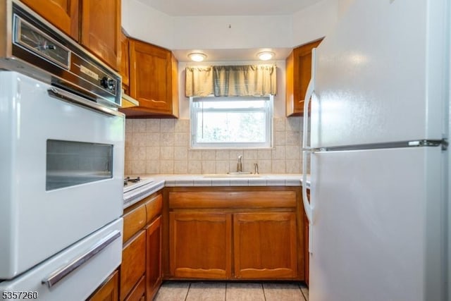 kitchen with white appliances, a sink, decorative backsplash, a warming drawer, and brown cabinetry