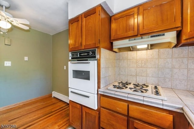 kitchen featuring white appliances, tile counters, ceiling fan, and under cabinet range hood
