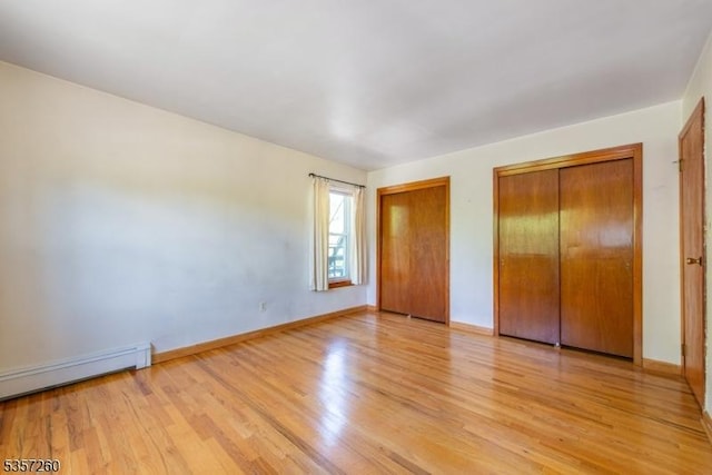 unfurnished bedroom featuring two closets, light wood finished floors, a baseboard radiator, and baseboards