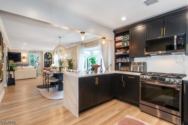 kitchen featuring stainless steel appliances, open floor plan, light wood finished floors, light countertops, and a peninsula
