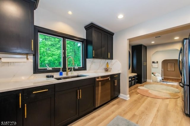 kitchen with stainless steel dishwasher, a sink, tasteful backsplash, light wood-style flooring, and freestanding refrigerator