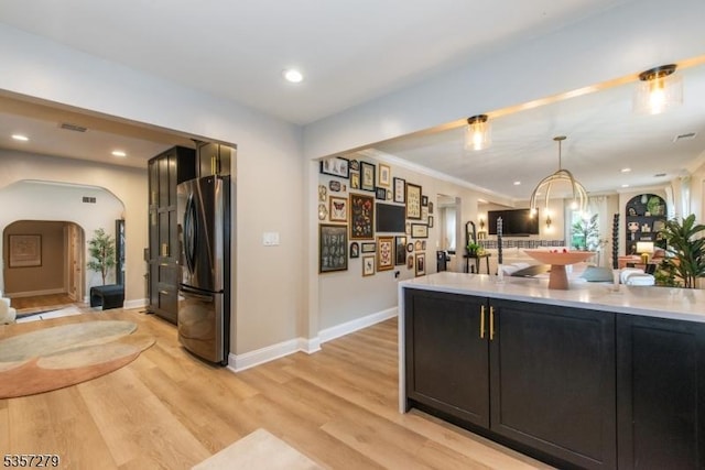 kitchen with freestanding refrigerator, arched walkways, light wood-type flooring, light countertops, and recessed lighting