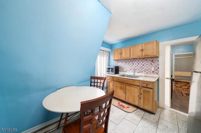 kitchen featuring a sink, stainless steel microwave, light countertops, decorative backsplash, and light tile patterned floors