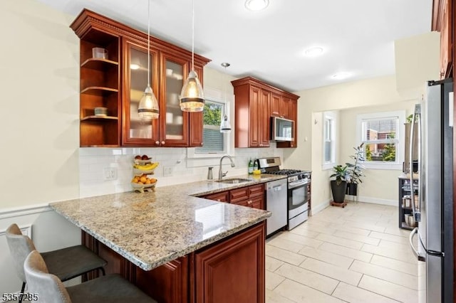 kitchen with a sink, appliances with stainless steel finishes, a peninsula, backsplash, and hanging light fixtures