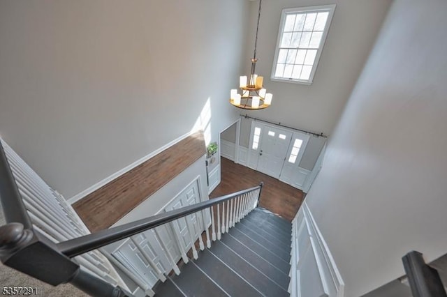 stairs featuring a chandelier, wood finished floors, and a high ceiling