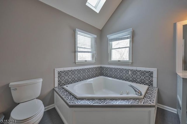 full bathroom featuring toilet, a skylight, baseboards, a garden tub, and high vaulted ceiling