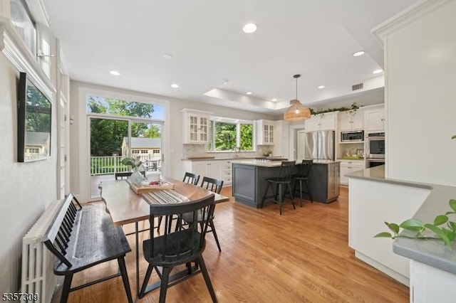 dining area with light wood-type flooring, recessed lighting, and a tray ceiling