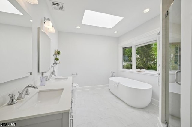 bathroom featuring a skylight, a freestanding bath, double vanity, a shower stall, and recessed lighting