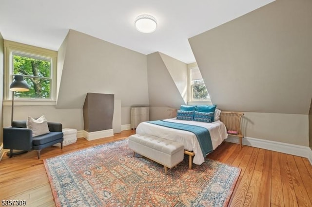 bedroom with radiator, light wood-style flooring, lofted ceiling, and baseboards