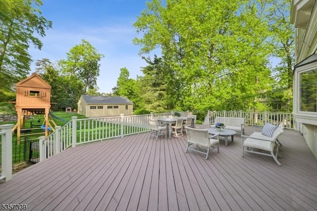 deck featuring a playground, outdoor dining space, an outbuilding, and a lawn