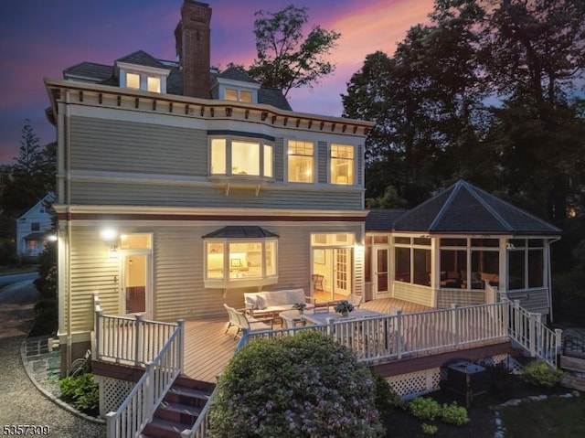 back of property featuring a sunroom, a chimney, a deck, and outdoor lounge area