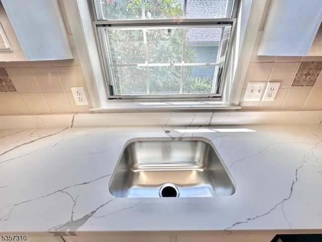 kitchen view of decorative backsplash, light stone counters, and a sink