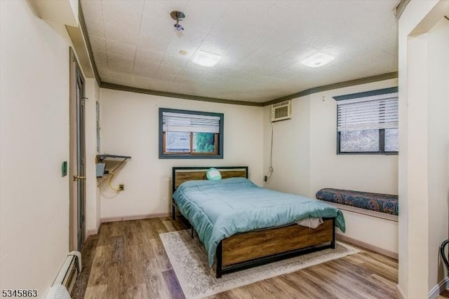 bedroom featuring wood finished floors, a baseboard heating unit, baseboards, ornamental molding, and a wall mounted AC