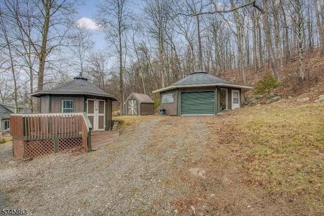 view of yard featuring an outbuilding, driveway, a garage, a storage unit, and a deck