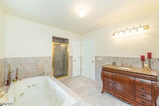 full bath with a stall shower, a tub with jets, tile walls, wainscoting, and vanity