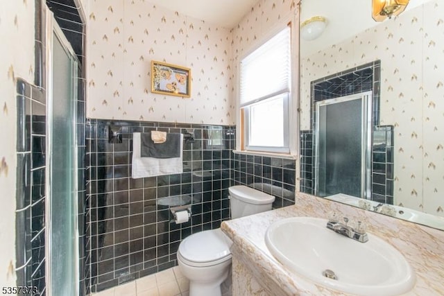 bathroom featuring wallpapered walls, tile walls, a stall shower, toilet, and wainscoting