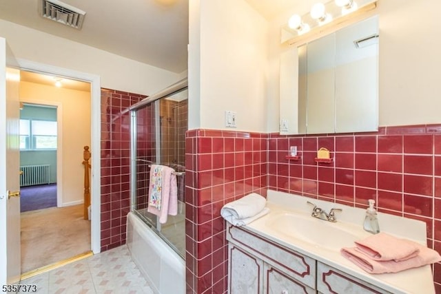 full bath with radiator heating unit, shower / bath combination with glass door, tile walls, vanity, and tile patterned floors