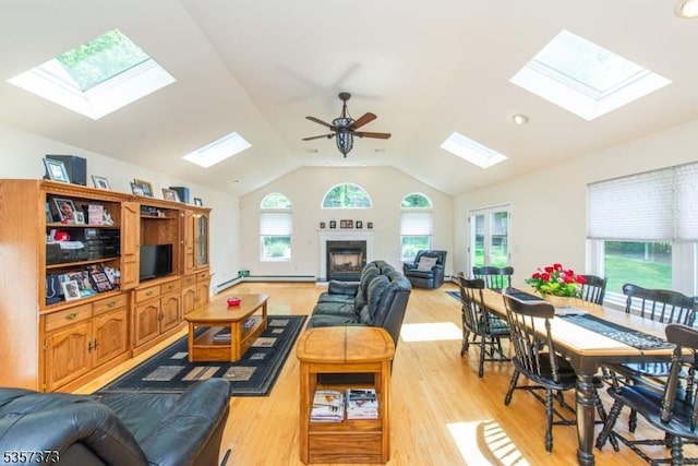 living area with a skylight, vaulted ceiling, light wood-style floors, and a ceiling fan
