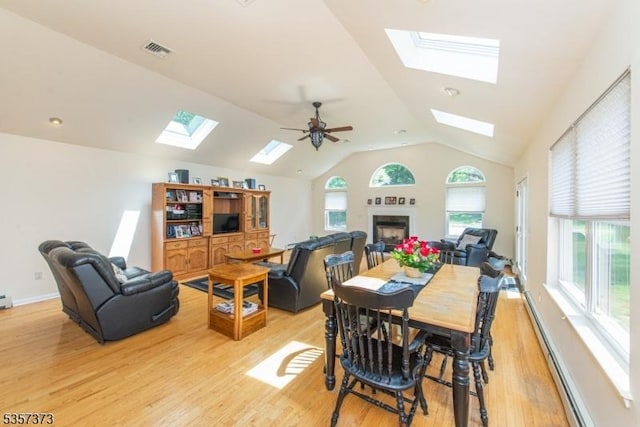 dining room with a skylight, light wood finished floors, lofted ceiling, a baseboard radiator, and ceiling fan