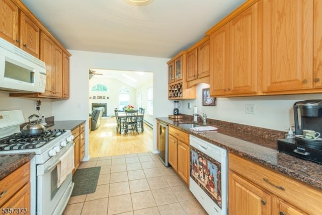 kitchen with white appliances, a sink, dark stone counters, light tile patterned flooring, and glass insert cabinets