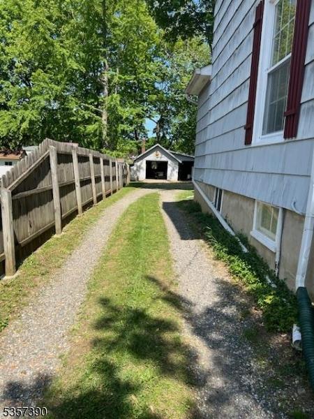 view of yard featuring dirt driveway, a garage, fence, and an outbuilding