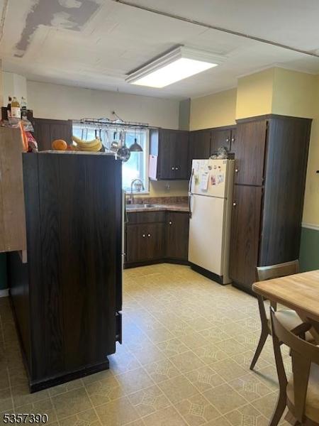 kitchen featuring freestanding refrigerator, dark brown cabinets, a sink, and light floors