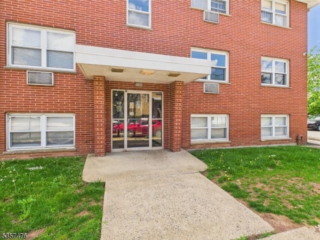 doorway to property featuring brick siding, a patio, and a lawn