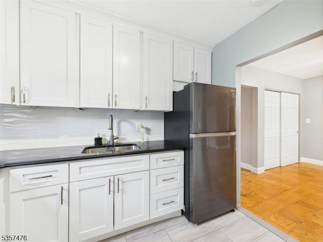 kitchen with a sink, freestanding refrigerator, backsplash, and white cabinetry
