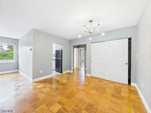unfurnished bedroom with freestanding refrigerator, a chandelier, baseboards, and a closet
