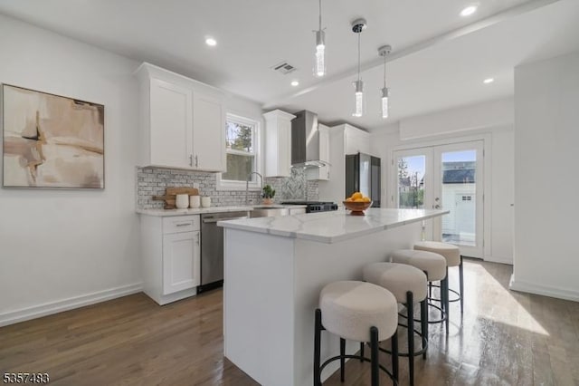 kitchen with dishwasher, wall chimney range hood, a breakfast bar, a kitchen island, and dark wood finished floors