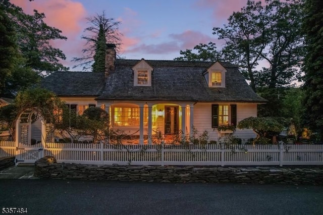 cape cod home featuring a fenced front yard and a chimney