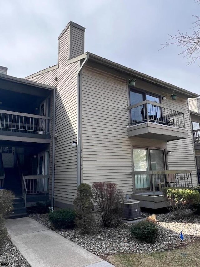 view of home's exterior with a balcony, a chimney, and central AC unit