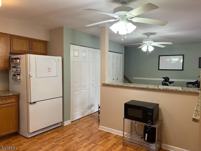 kitchen with freestanding refrigerator, black microwave, brown cabinetry, light wood-style flooring, and a ceiling fan