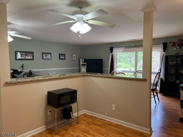 kitchen featuring black microwave, a ceiling fan, wood finished floors, and light stone countertops