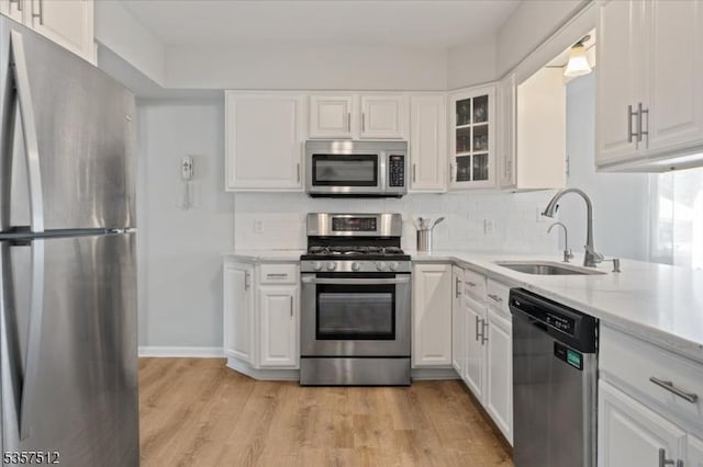 kitchen featuring appliances with stainless steel finishes, a sink, white cabinetry, and light wood-style flooring