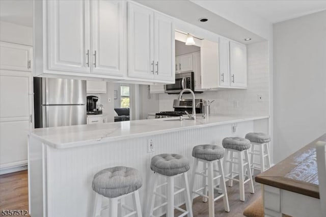 kitchen with appliances with stainless steel finishes, white cabinets, light wood-type flooring, a peninsula, and light countertops