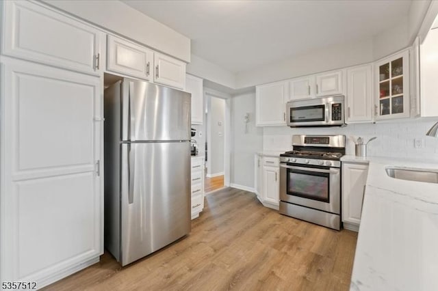 kitchen with appliances with stainless steel finishes, a sink, white cabinetry, glass insert cabinets, and light stone counters