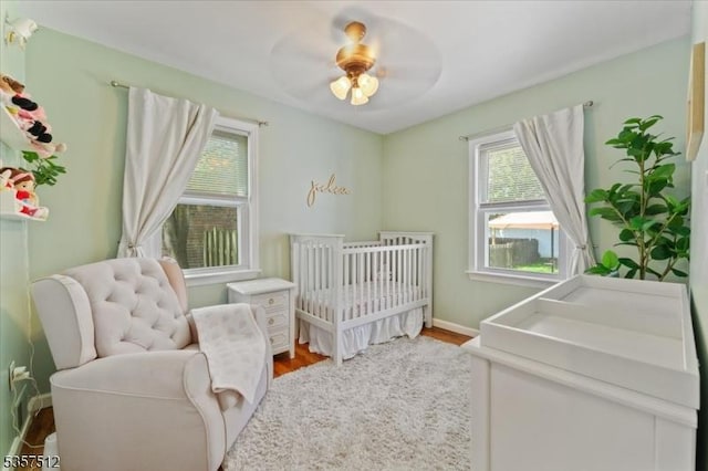 bedroom featuring a nursery area, wood finished floors, ceiling fan, and baseboards