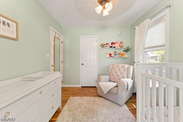 bedroom with a crib, wood finished floors, baseboards, and a ceiling fan