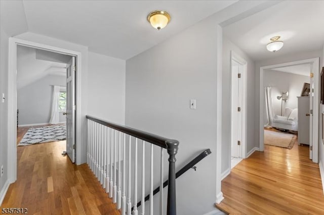 hallway with an upstairs landing, light wood-style flooring, lofted ceiling, and baseboards