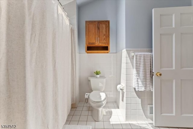 full bathroom with tile patterned flooring, tile walls, toilet, and wainscoting