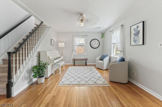 living area with stairs, a ceiling fan, wood finished floors, and baseboards