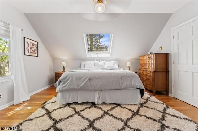 bedroom with lofted ceiling, light wood-type flooring, baseboards, a skylight, and a ceiling fan