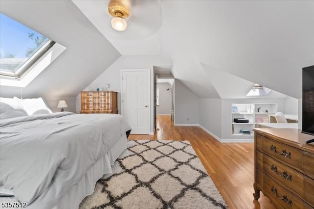bedroom featuring vaulted ceiling, light wood-style flooring, a skylight, baseboards, and a ceiling fan