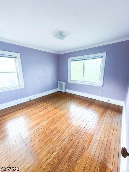 spare room featuring wood-type flooring, ornamental molding, and baseboards