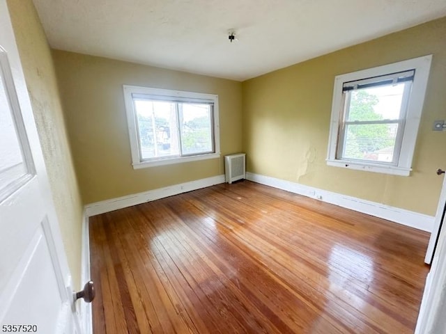 empty room featuring plenty of natural light, hardwood / wood-style floors, and baseboards