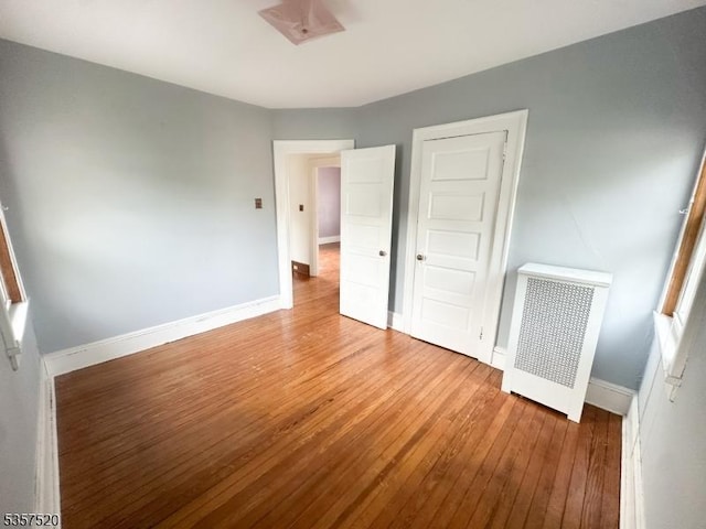 unfurnished bedroom with wood-type flooring, radiator, and baseboards