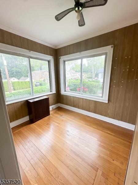 unfurnished room with light wood-style flooring, ceiling fan, baseboards, and wood walls