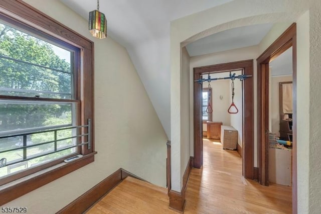 hallway featuring light wood-type flooring, an upstairs landing, and arched walkways
